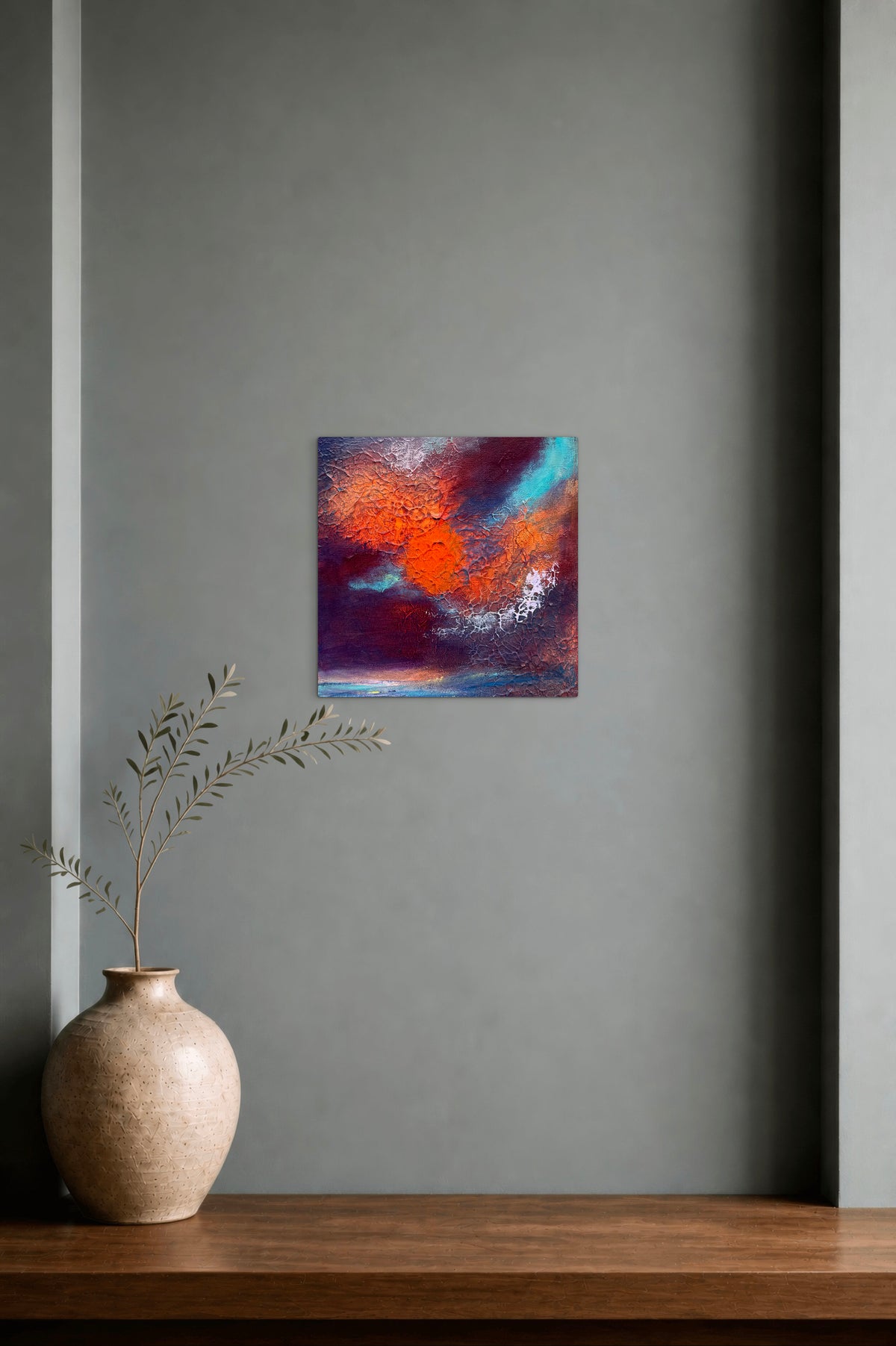 Abstract wall art featuring vibrant orange, red, blue, and purple brushstrokes, displayed on a gray wall above a wooden shelf with a ceramic vase and dried branches.