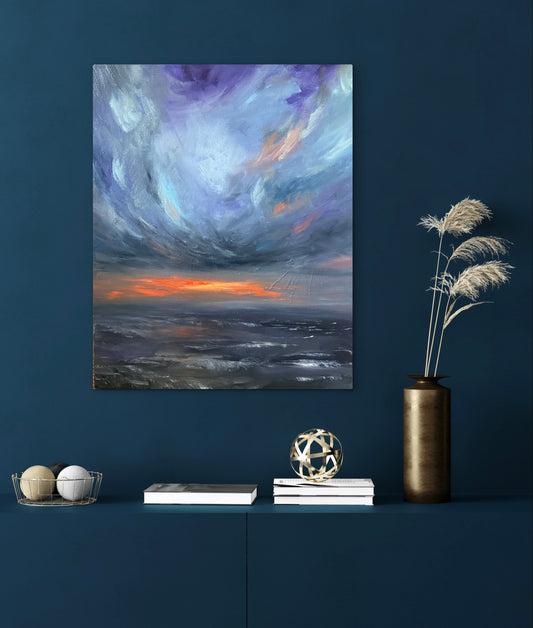 An abstract canvas painting of a dramatic storm sky with purple, blue, gray, and orange clouds, displayed on a dark blue wall above a shelf with decorative books, a vase, and dried grass.