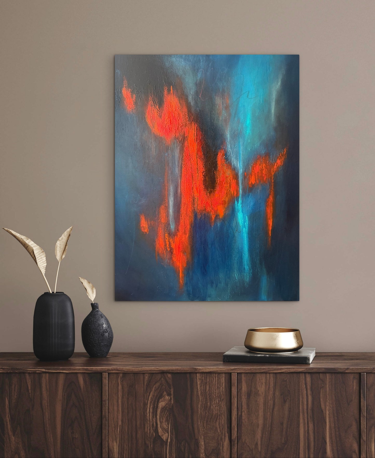 Abstract canvas wall art featuring bold blue and orange brushstrokes, displayed on a beige wall above a dark wood console table with decorative vases and a gold bowl.
