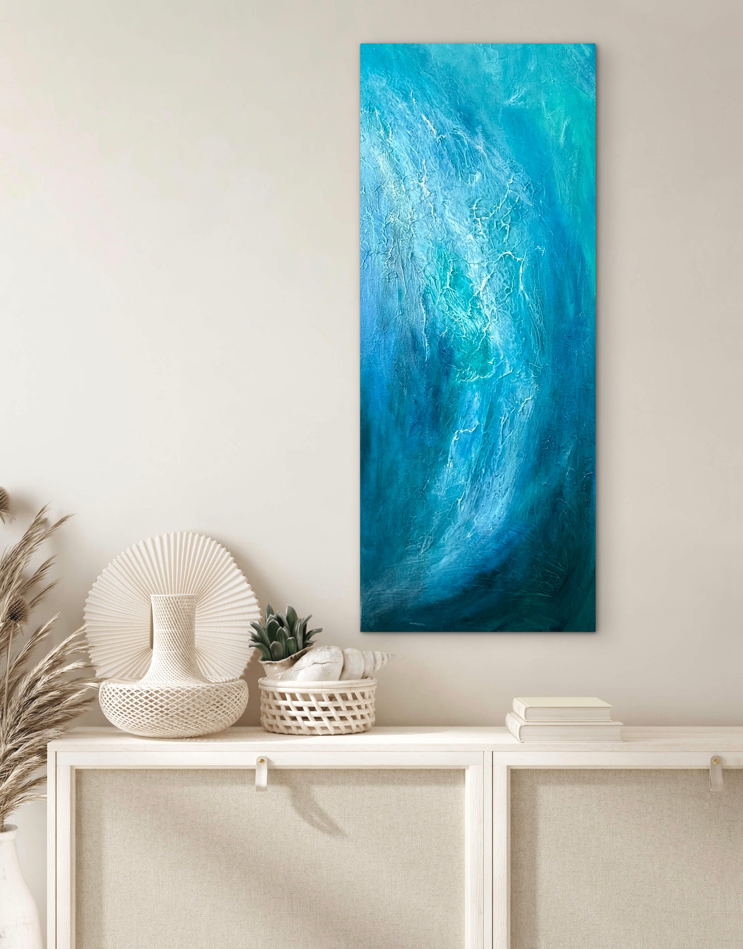 A vertical abstract canvas painting featuring a swirling wave-like pattern in shades of blue and teal, displayed on a light beige wall above a white console table with decorative items.