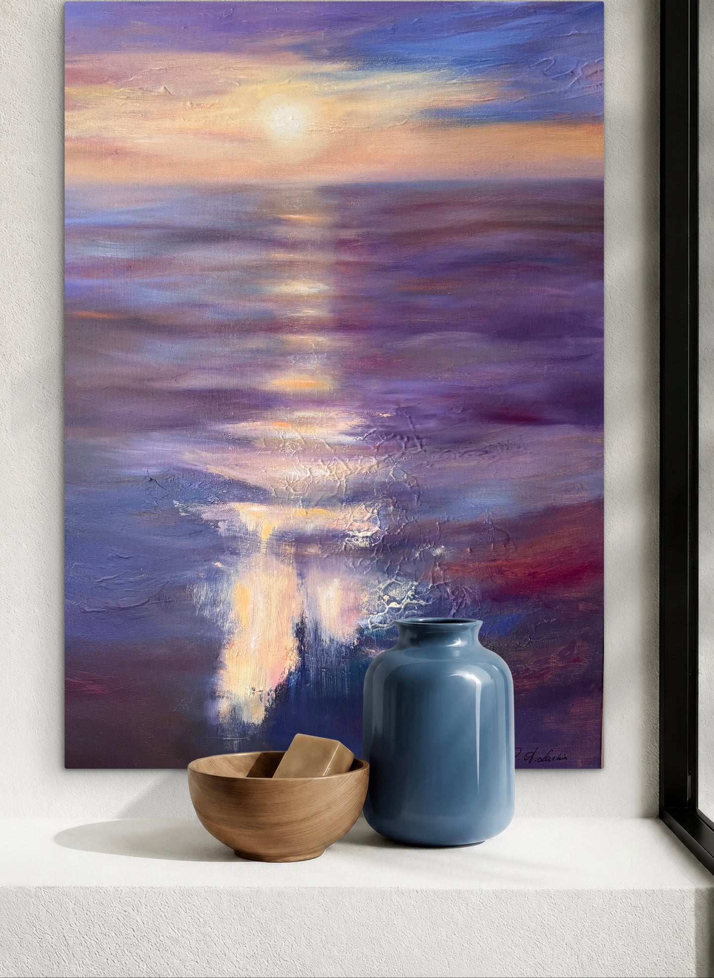 A vertical canvas painting of a sunset over water, featuring blended hues of purple, blue, orange, and gold. The painting is displayed on a white wall above a white windowsill, styled with a small wooden bowl and a blue ceramic vase.