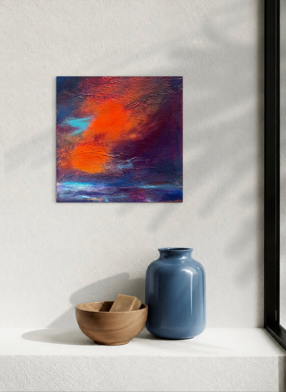 An abstract canvas painting with vibrant orange, red, and deep purple brushstrokes, displayed on a white wall above a shelf with a blue vase and a wooden bowl.